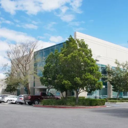 A modern office building stands prominently with red landscaping and parked trucks along a paved street in Fontana California
