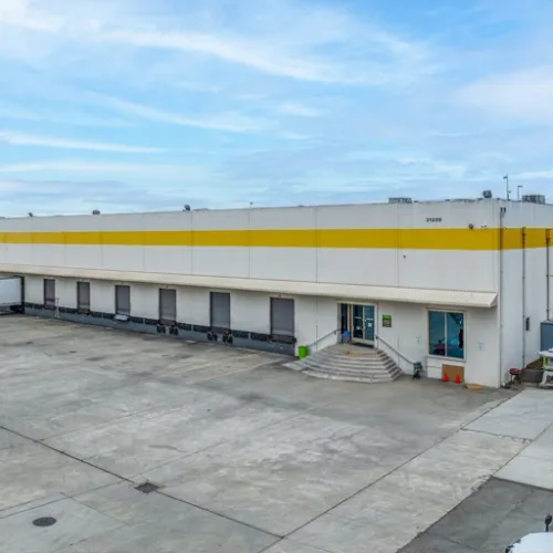 A large industrial building with a yellow stripe and white exterior dominates the scene featuring concrete pavement and steps