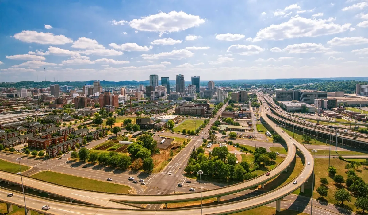 A sweeping aerial view showcases a multilane highway cutting through a green landscape with residential areas and buildings