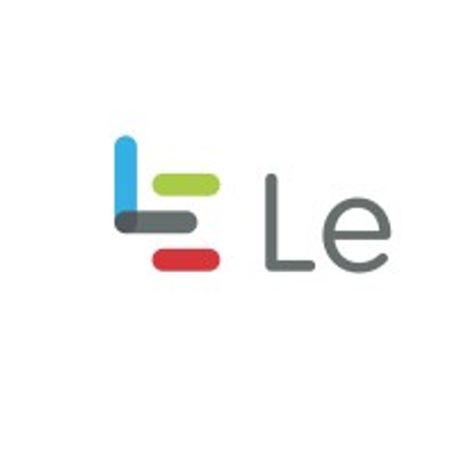 Le Creuset of America logo featuring a stylized segmented shield in red gray and white with a central gold accent