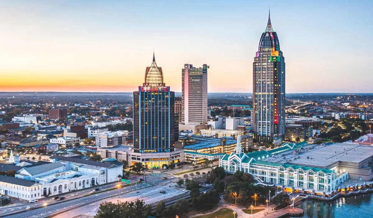Tall skyscrapers dominate an aerial view of Mobile Alabama illuminated at dusk A modern waterfront scene features historic