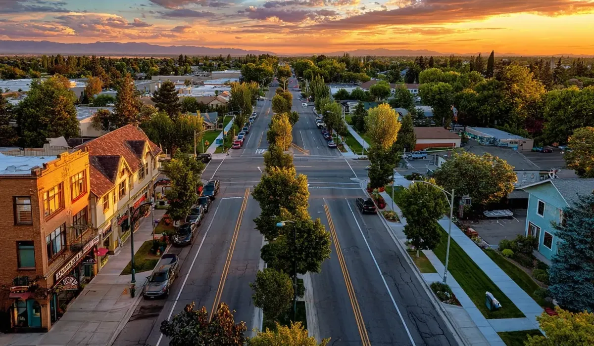 A wide street stretches through Nampa Idaho lined with mature trees and sidewalks offering a view of residential buildings