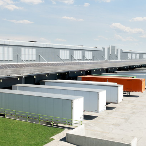 A large industrial complex features numerous gray shipping containers and a green lawn area The scene showcases a commercial