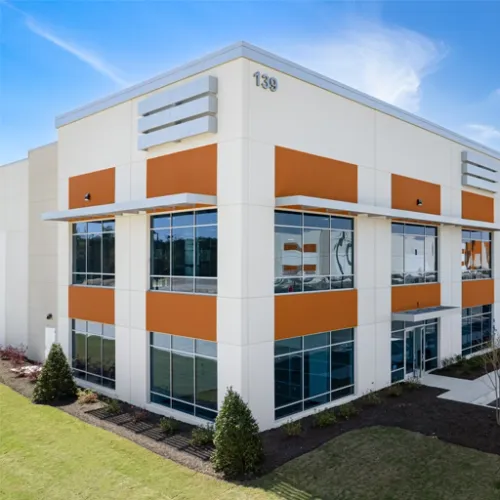 A modern orange and white building stands prominently with landscaping and greenery surrounding its base